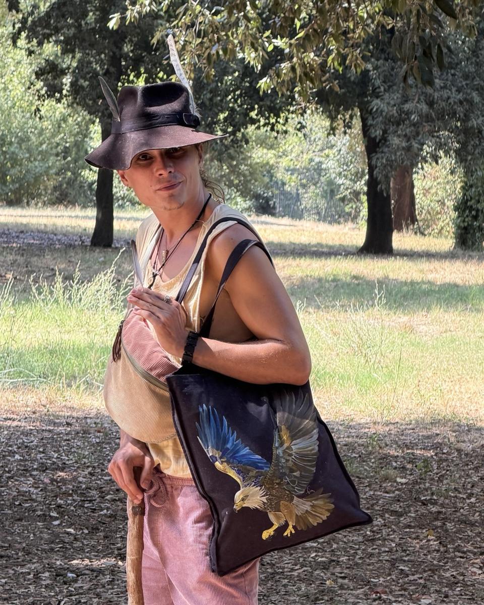 Manuel Keller in a park, wearing a feathered hat